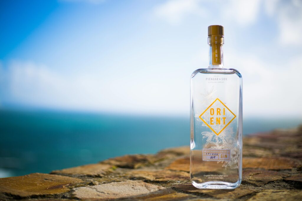 A clear gin bottle with elegant design in front of a scenic ocean backdrop.